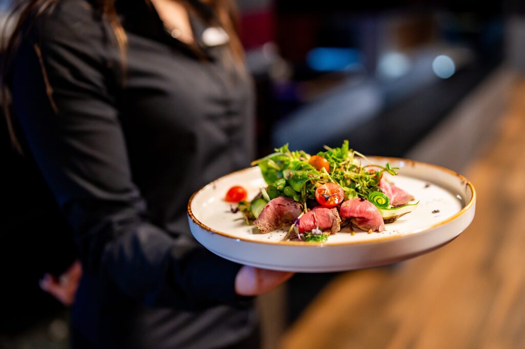 Person holding a plate of gourmet salad with seared tuna. The image captures the art of fine dining and beautifully presented dish